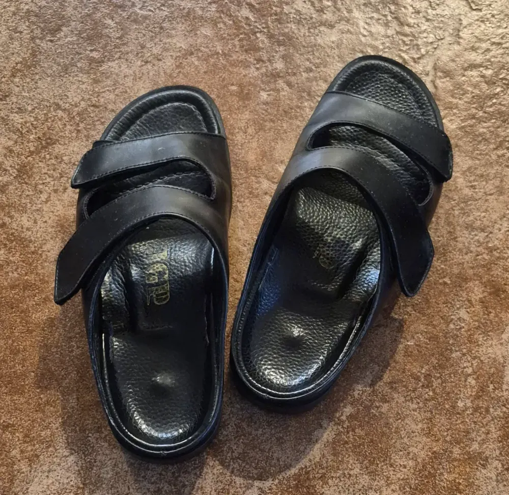 A pair of black JGP leather slippers with two adjustable straps, like the pair she tried on in our Tucson store